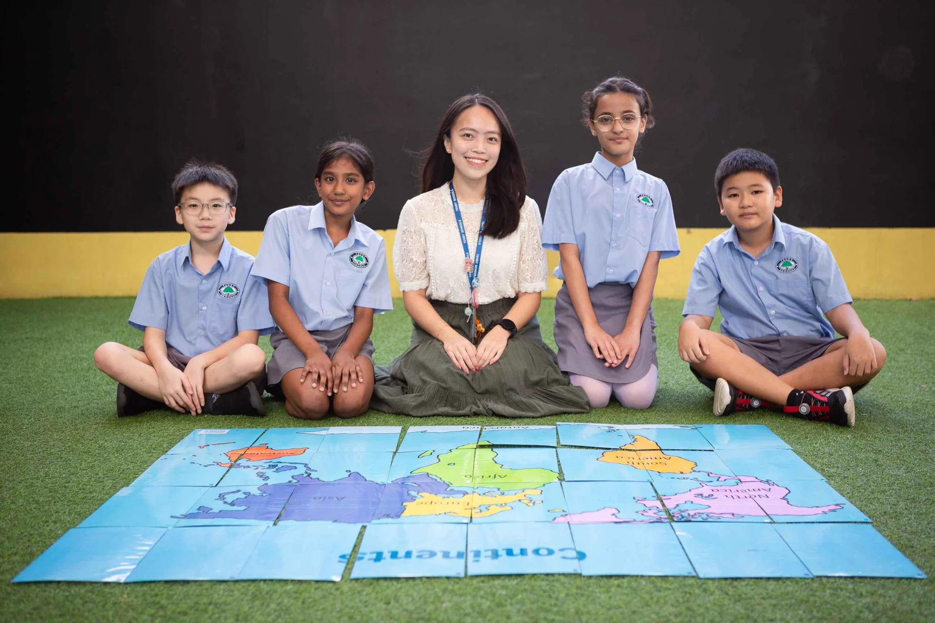 Students and their teacher smiling while sitting, with a map on the floor