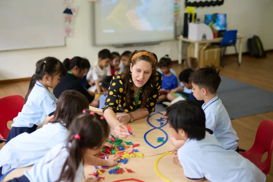 Teacher engages young students with colorful toys at a classroom table, fostering learning and creativity in an interactive setting.