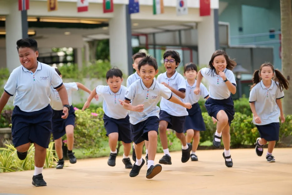 Children in uniforms joyfully run outdoors, surrounded by greenery and international flags, embodying school spirit and unity.