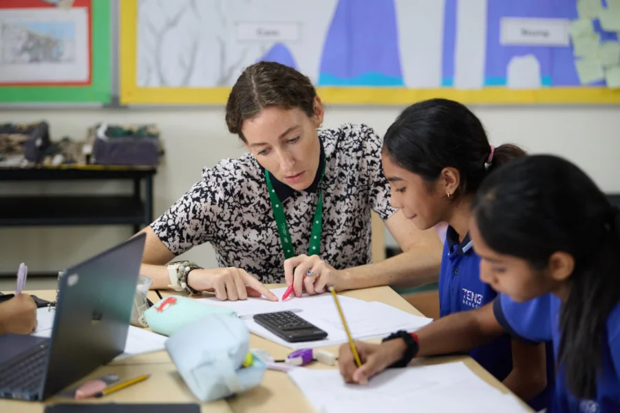 A teacher attentively helps two students with their schoolwork in a classroom setting.